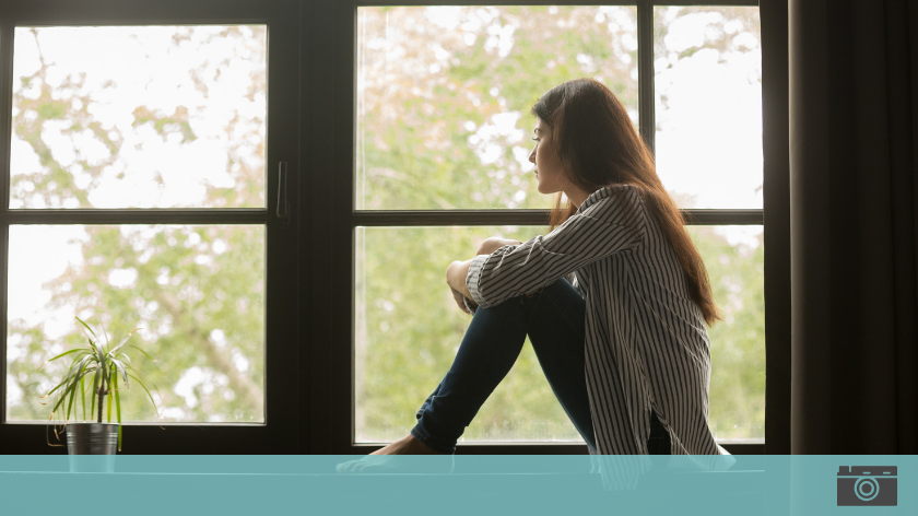 Woman in window contemplating the cost of loneliness - Vitality