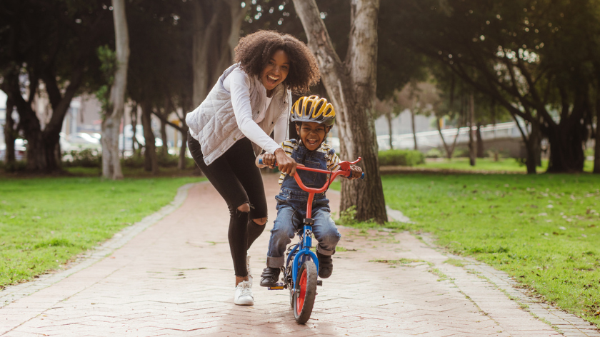 Mother helps son learn how to ride bike smiling outdoors for family fitness- Vitality