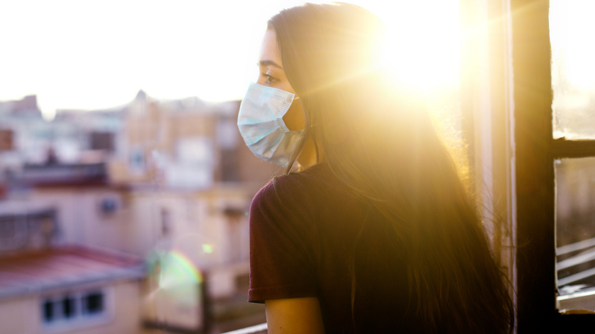 woman in face mask looking out window - vitality