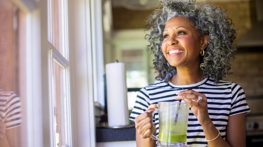 Woman smiling and drinking green healthy smoothie at home - Vitality