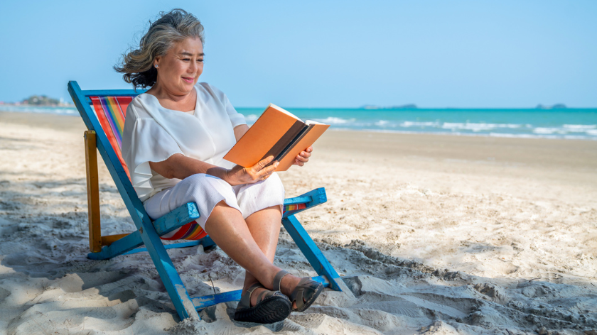 Senior woman reading on beach making time during summer seasons - Vitality - Vitality