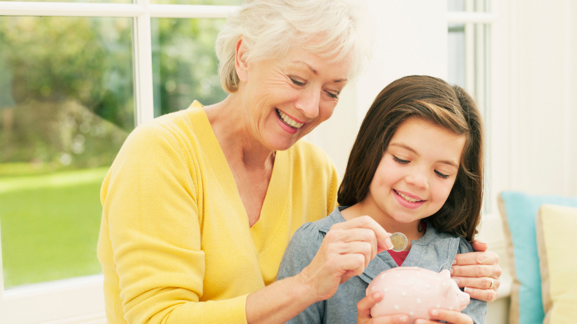 Grandmother and granddaughter putting money in piggybank for emergency savings - Vitality