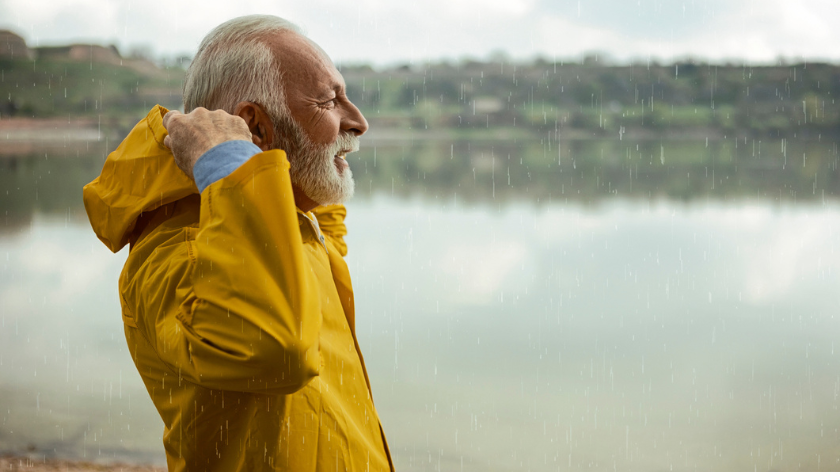 Senior man in raincoat outdoors protecting self from rain - Vitality