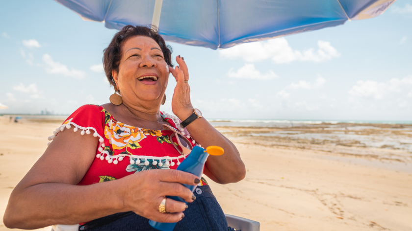 Senior woman on beach putting on sunscreen to stay safe- Vitality