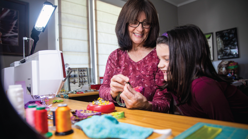 Woman sewing a face mask at home with a young girl - Vitality