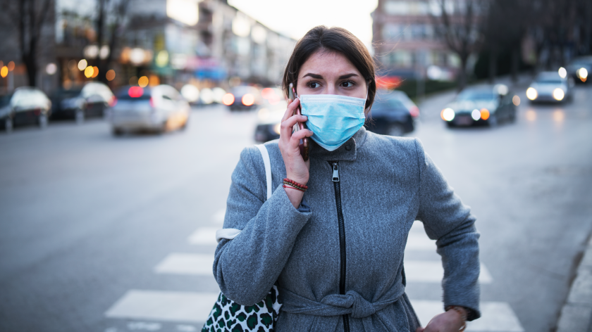 Woman in mask on city crosswalk talking on cell phone - Vitality