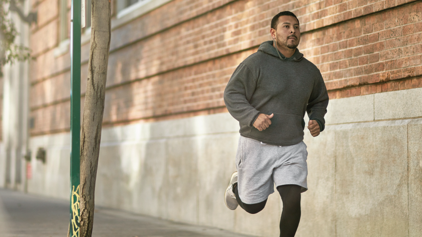 Man running outdoors in hooded sweatshirt during pandemic - Vitality