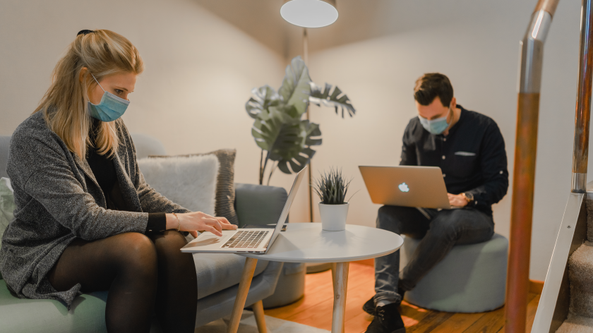 Coworkers wearing masks working on laptops in shared space - Vitality