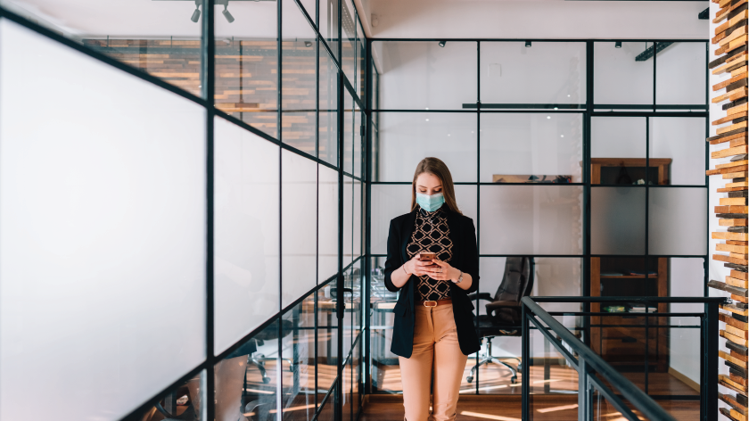 Woman at workplace using phone wearing a face mask - Vitality