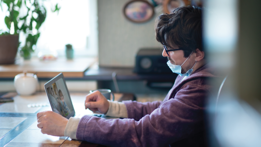 Fatigued man in virtual meeting on laptop with face mask down - Vitality