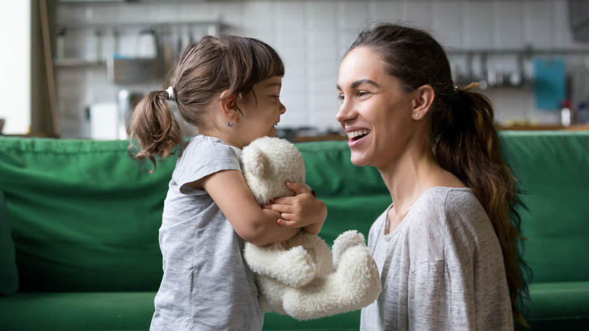 Mom and daughter smiling at home with teddy bear for staying positive - Vitality