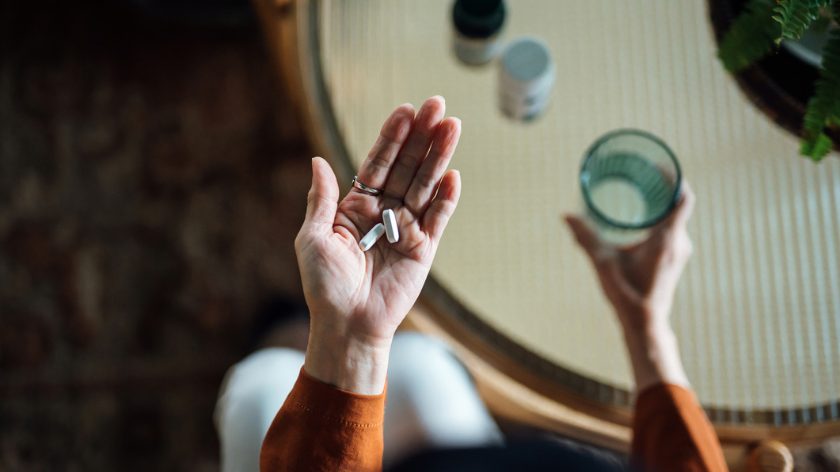 Woman holds routine daily health supplements and glass of water in hand - Vitality