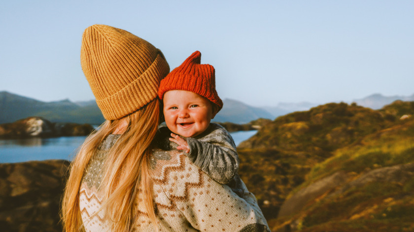 Woman holding baby outdoors smiling for mental health - Vitality