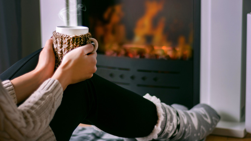 Woman drinking warm beverage from a mug by fire - Vitality